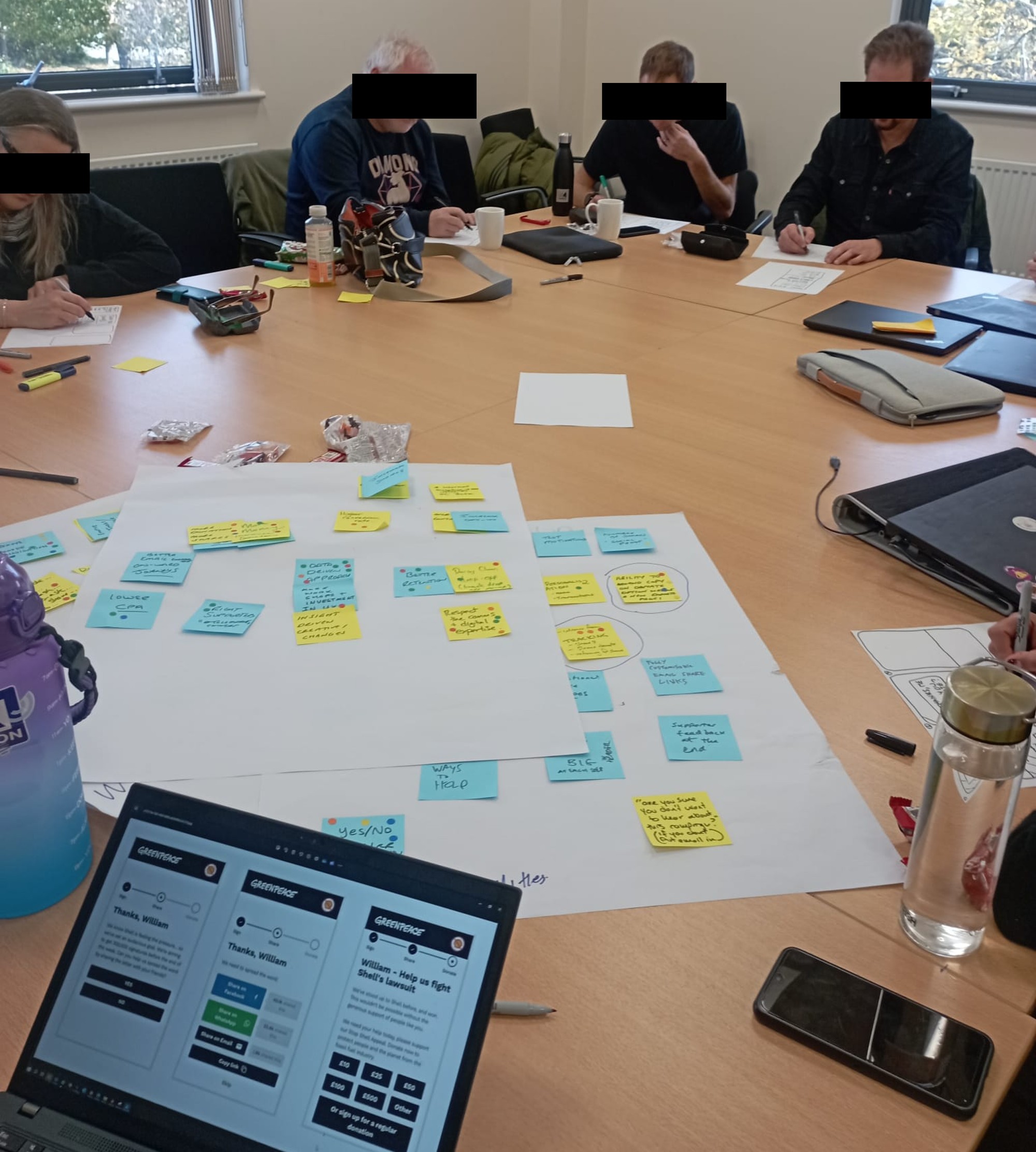A co-design workshop session around a table, sorting sticky notes into themes while reviewing a donation flow prototype on a laptop
